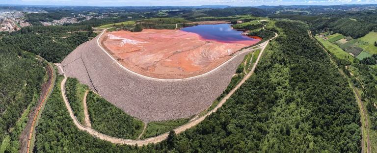 Vista aérea de uma barragem em processo de descaracterização, com maquinário pesado removendo o material de contenção, enquanto a vegetação começa a se regenerar na área circundante